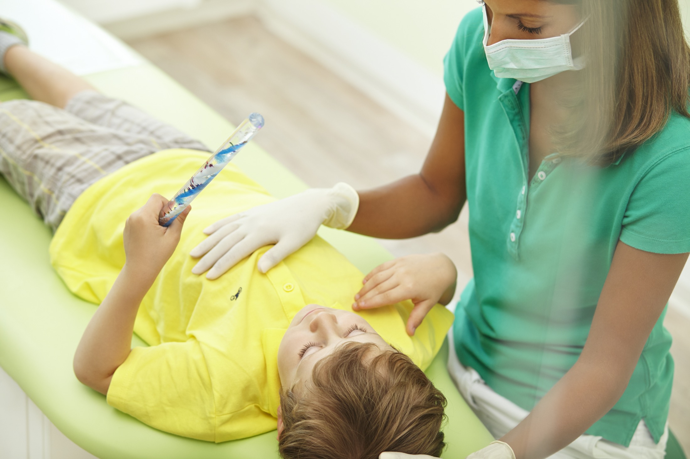 Junger Patient liegt auf der Liege. Zahnärztin sitzt daneben